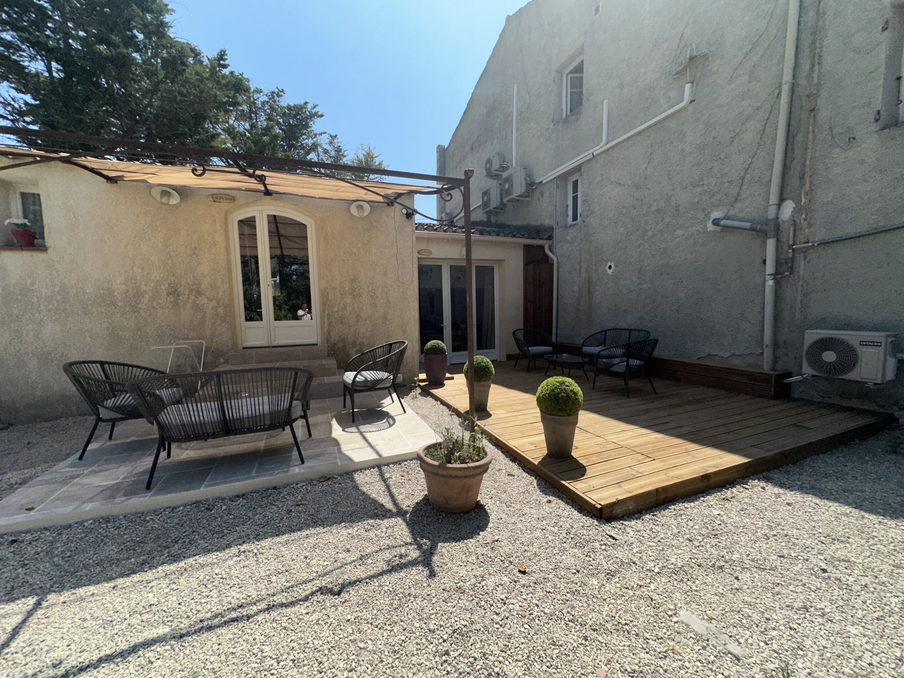 Un patio con mobiliario exterior, una construcción pequeña y una terraza de madera.