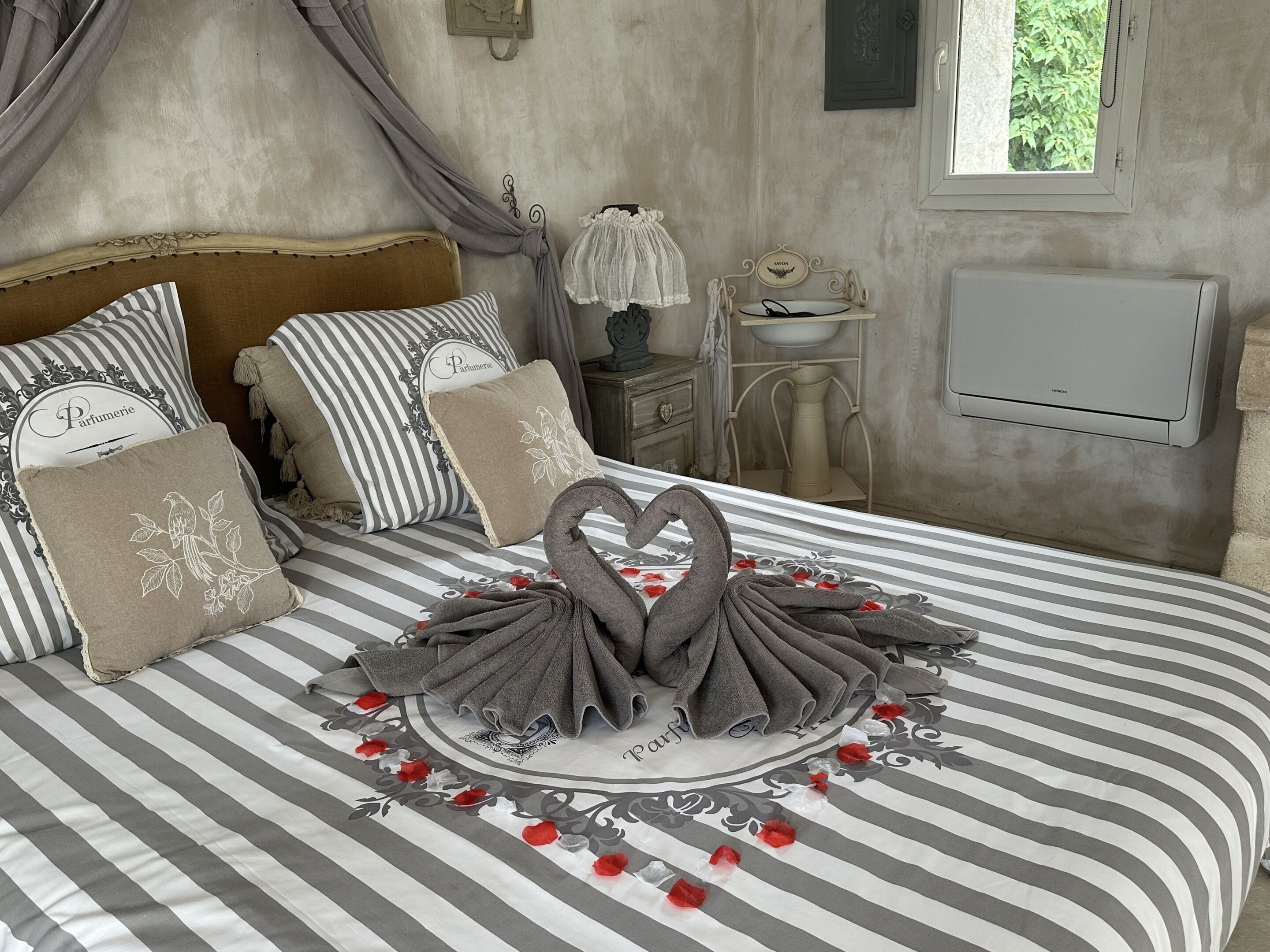 A neatly made bed with striped bedding, decorative pillows, and a swan-shaped towel arrangement.