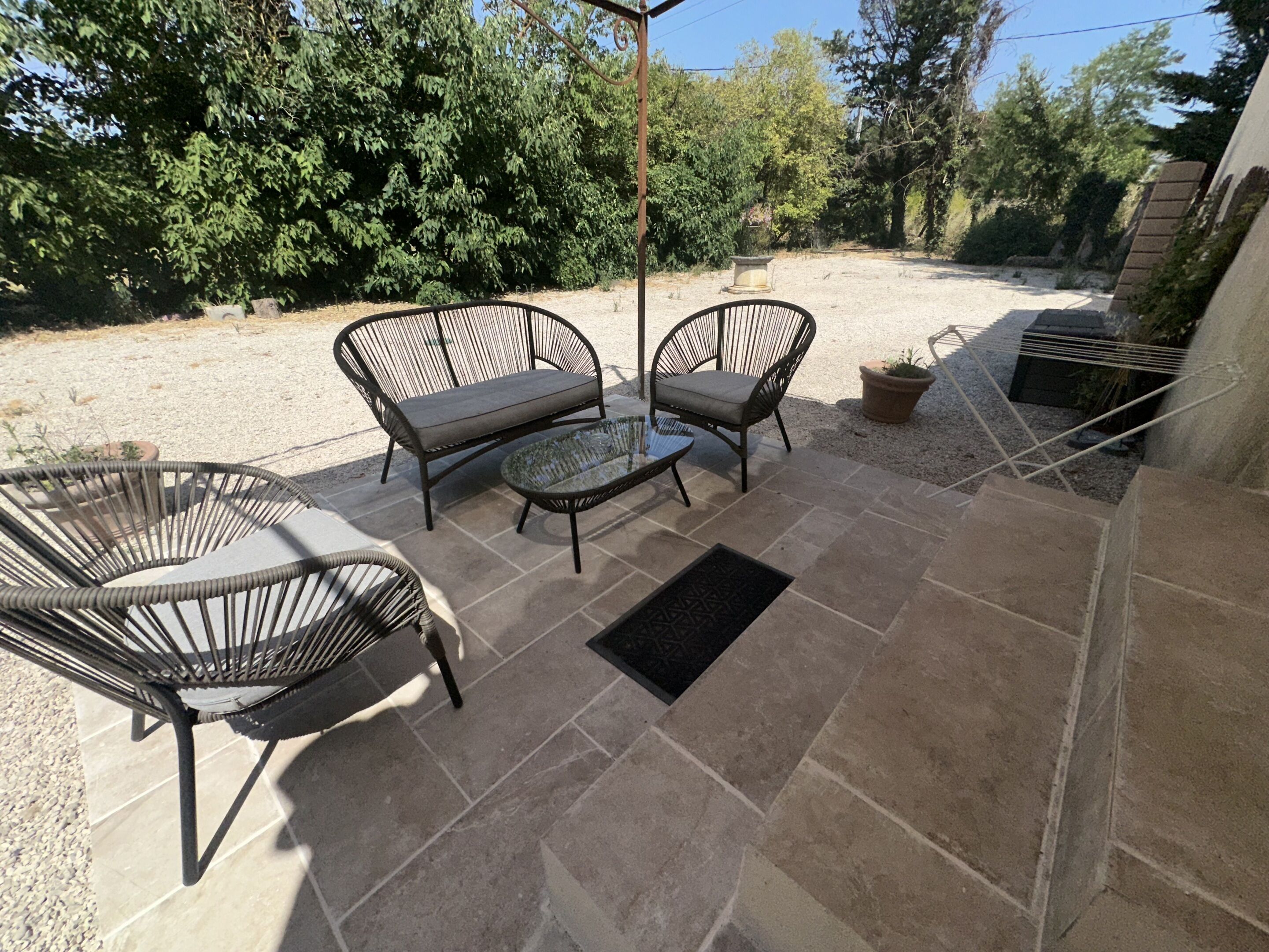 Um pátio externo com móveis de vime, uma mesa de vidro e piso de pedra.
