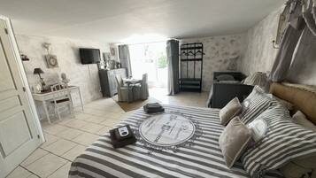 Un dormitorio con cama, mesita de noche y escritorio con silla. Hay una ventana con cortinas, un televisor en la pared y una puerta.