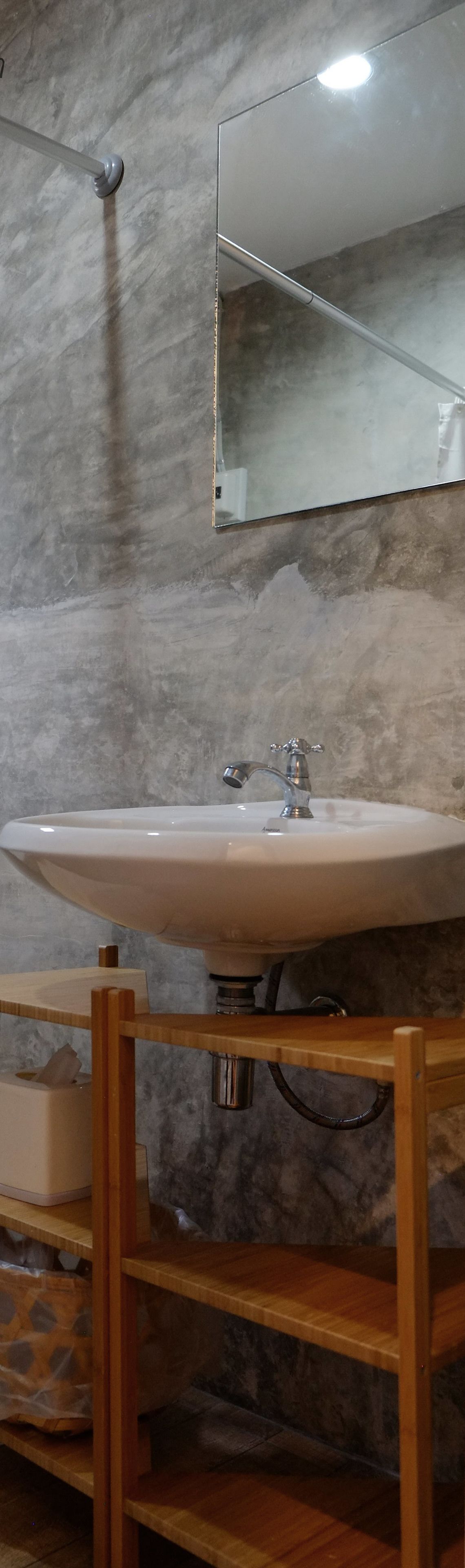 Un baño con un lavamanos blanco, un espejo encima y un estante de madera debajo.
