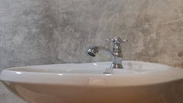 Un baño con un lavamanos blanco, un espejo encima y un estante de madera debajo.
