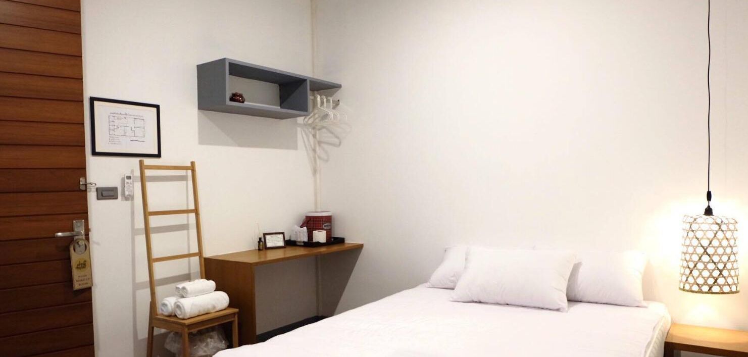Habitación de hotel con cama, escalera de madera, repisa con artículos de aseo, mapa enmarcado y lámpara colgante.