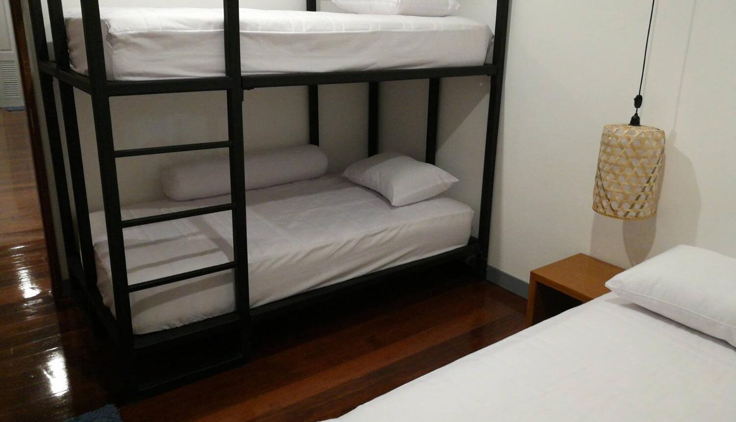 Una litera con ropa de cama blanca, una mesita de noche de madera y una lámpara colgante.