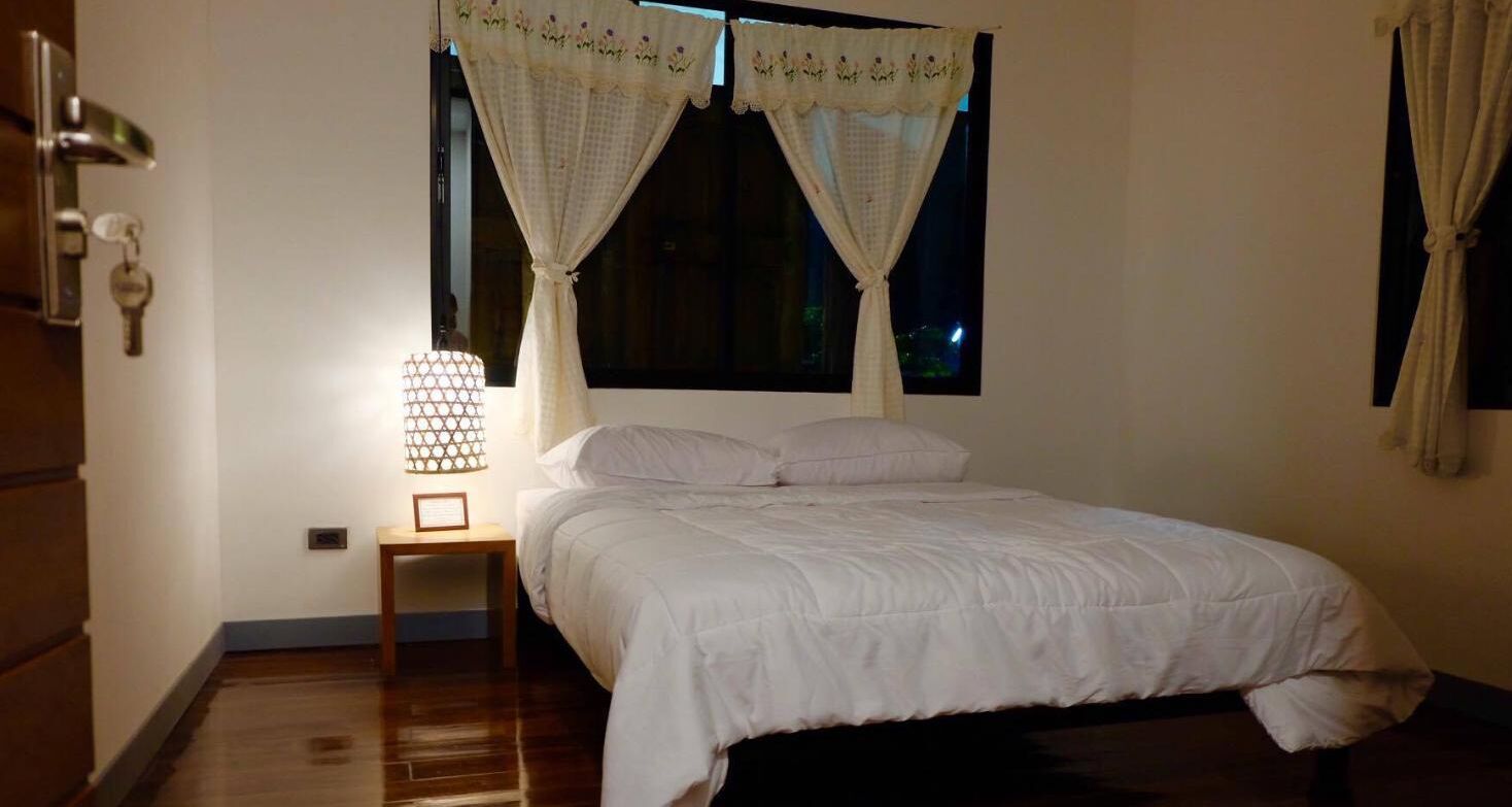A bedroom with a bed, a nightstand with a lamp, and a window with curtains.
