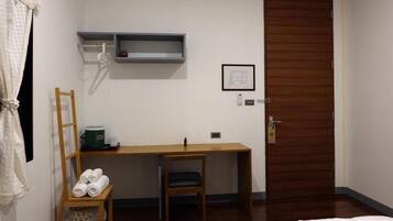 A bedroom with a wooden desk, a chair, a bed, a wooden wardrobe, and a small shelf with a vase.
