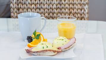 Un plato de desayuno con huevos Benedict, rodajas de naranja y un vaso de zumo de naranja sobre un mantel blanco.