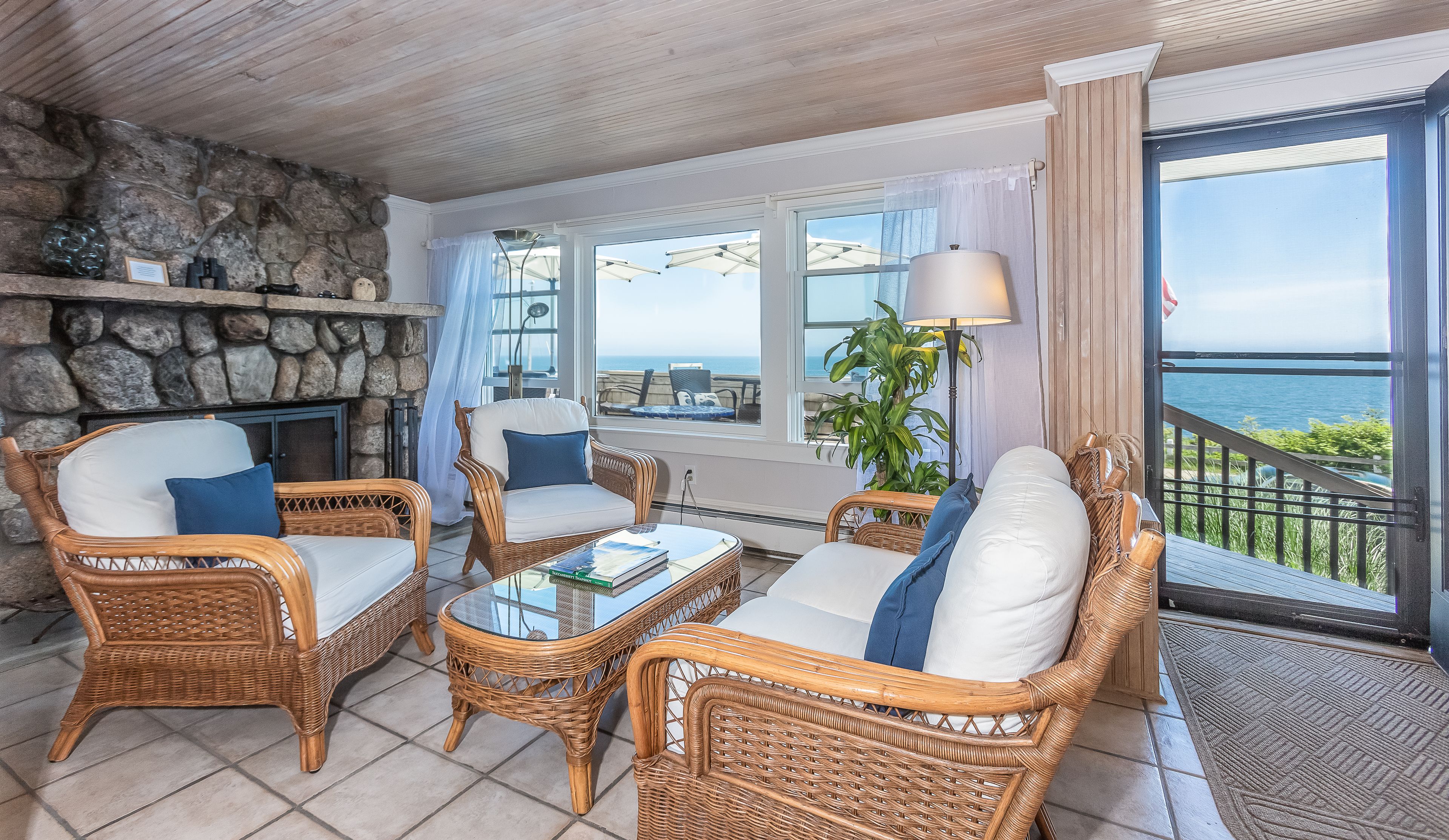 A cozy room with wicker furniture, a glass table, and a stone wall.