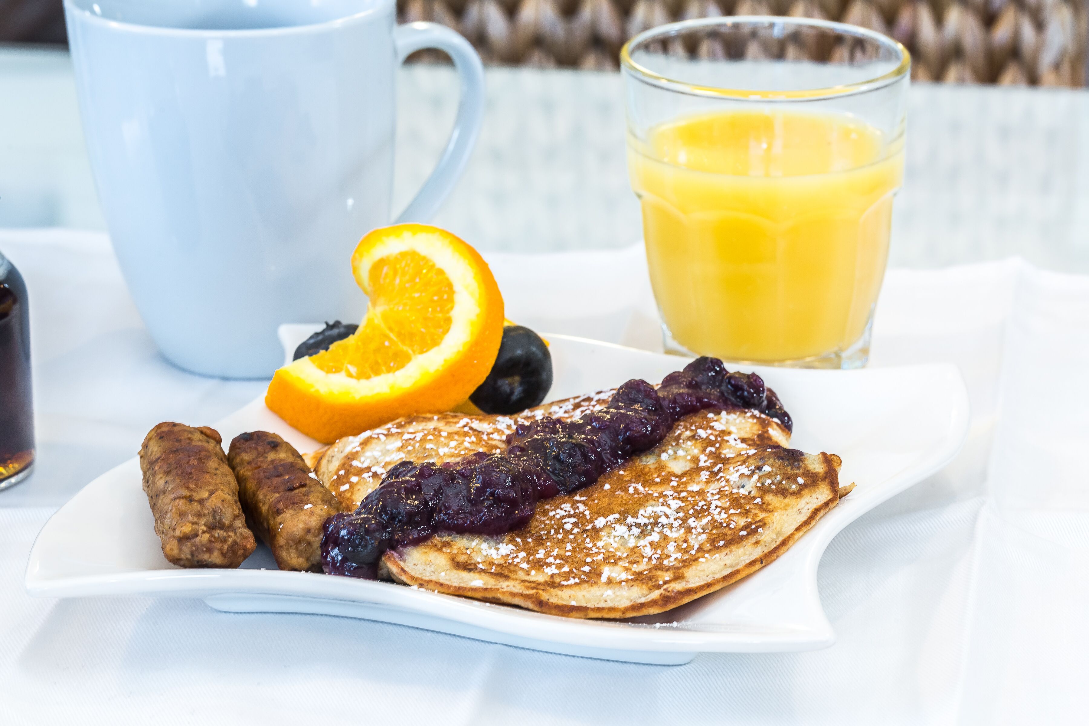 A breakfast plate with pancakes, sausage, and fruit, accompanied by a glass of orange juice and a cup.