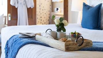 A neatly made bed with a tray of breakfast items, a vase of flowers, and a robe hanging on the door.