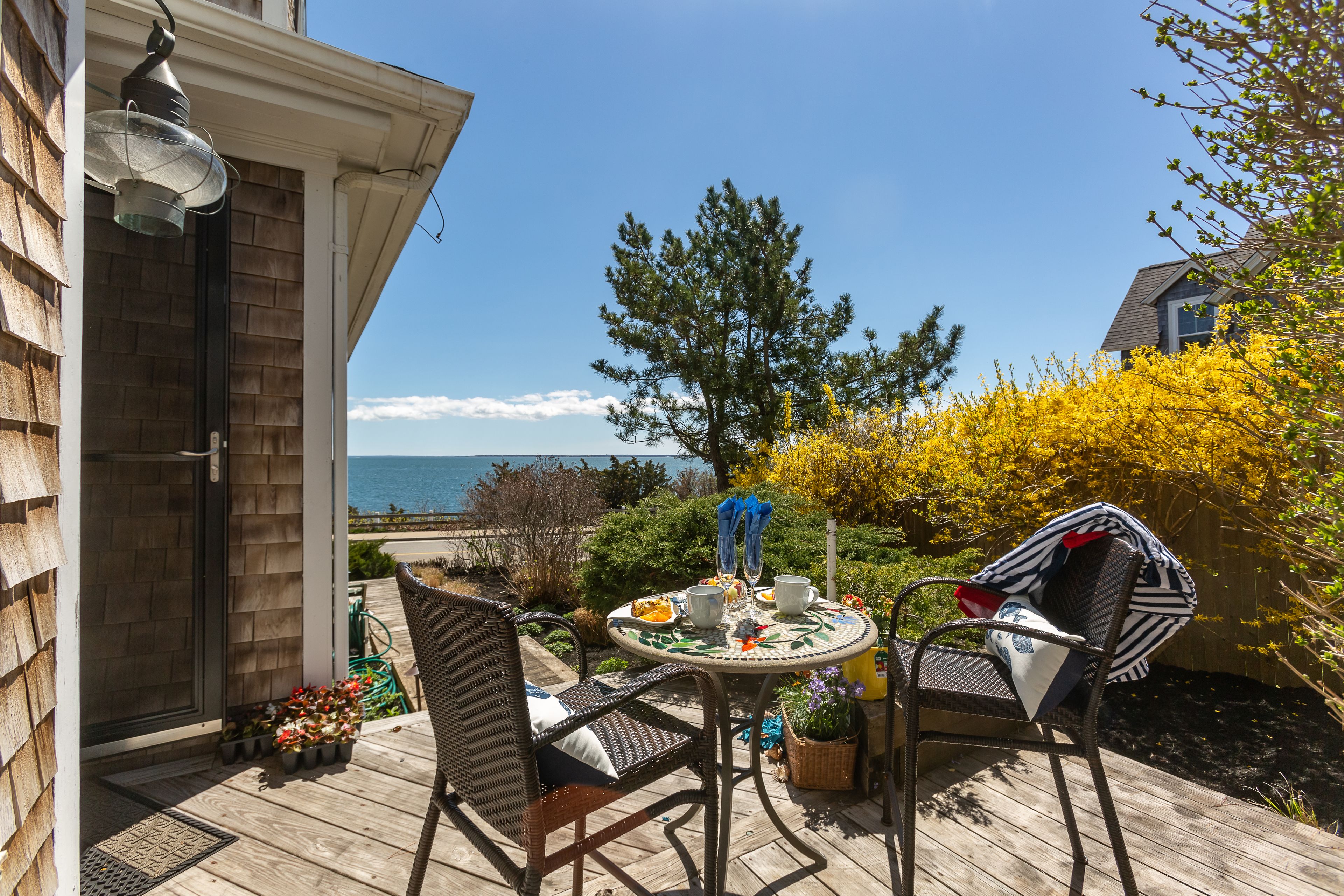 A wooden deck with outdoor furniture, a table set for dining, and a view of the sea.