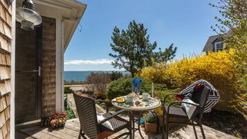 A wooden deck with outdoor furniture, a table set for dining, and a view of the sea.