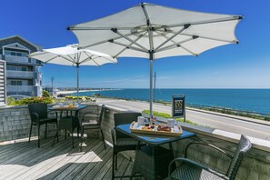 A seaside patio with outdoor seating, umbrellas, and a view of the ocean.