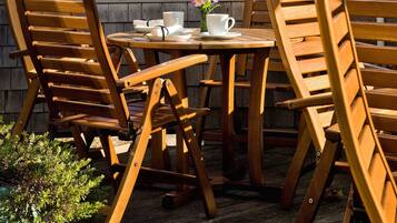 A wooden outdoor table and chairs with a white umbrella, set against a backdrop of a residential building with balconies.