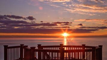 Een zonsondergang boven een wateroppervlak met een houten balustrade op de voorgrond.