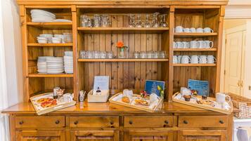 A wooden buffet setup with trays of food, glassware, and plates.