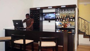 A bar area with a bartender, a television mounted above the bar, and a wine and liquor shelf. - Lakeem Suites Adebola (Lagos)