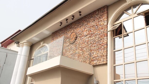 A building facade with a stone wall, a large arched window, and a balcony with a railing. - Lakeem Suites Adebola (Lagos)