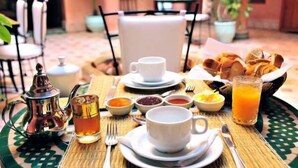 A breakfast setting with a teapot, cups, a glass of orange juice, and a basket of croissants on a table. - Riad BenSaid (Marrakech)