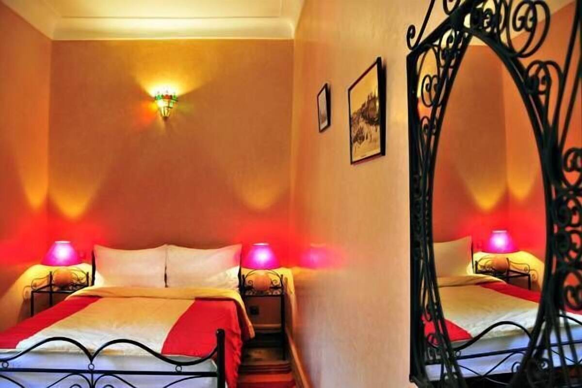 Quarto de hotel com duas camas, uma escada, luminária fixada na parede e um arco metálico decorativo.
