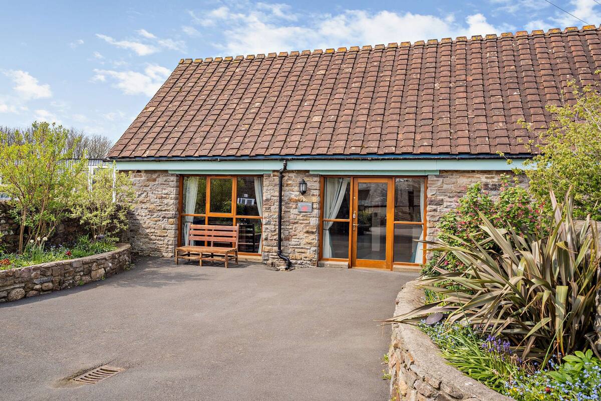 A stone building with a tiled roof, large glass doors, and a bench outside.