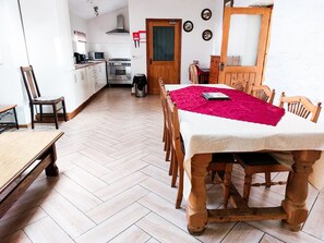 A dining area with a wooden table and chairs, a red table runner, and a kitchen in the background.