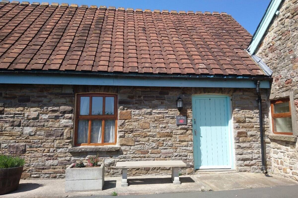 A stone building with a tiled roof, a wooden door, and a bench outside.