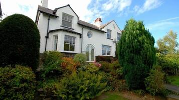 A white two-story house with a well-maintained garden, including a variety of shrubs and a tall conifer.