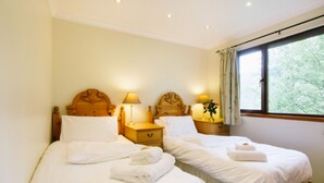 A hotel room with two single beds, each with a wooden headboard, bedside tables with lamps, and a window with a view of trees. - The Buzzard (Crianlarich)