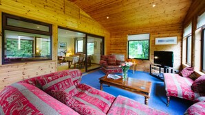 A cozy cabin interior with a large sofa, a coffee table, and a TV. - The Buzzard (Crianlarich)