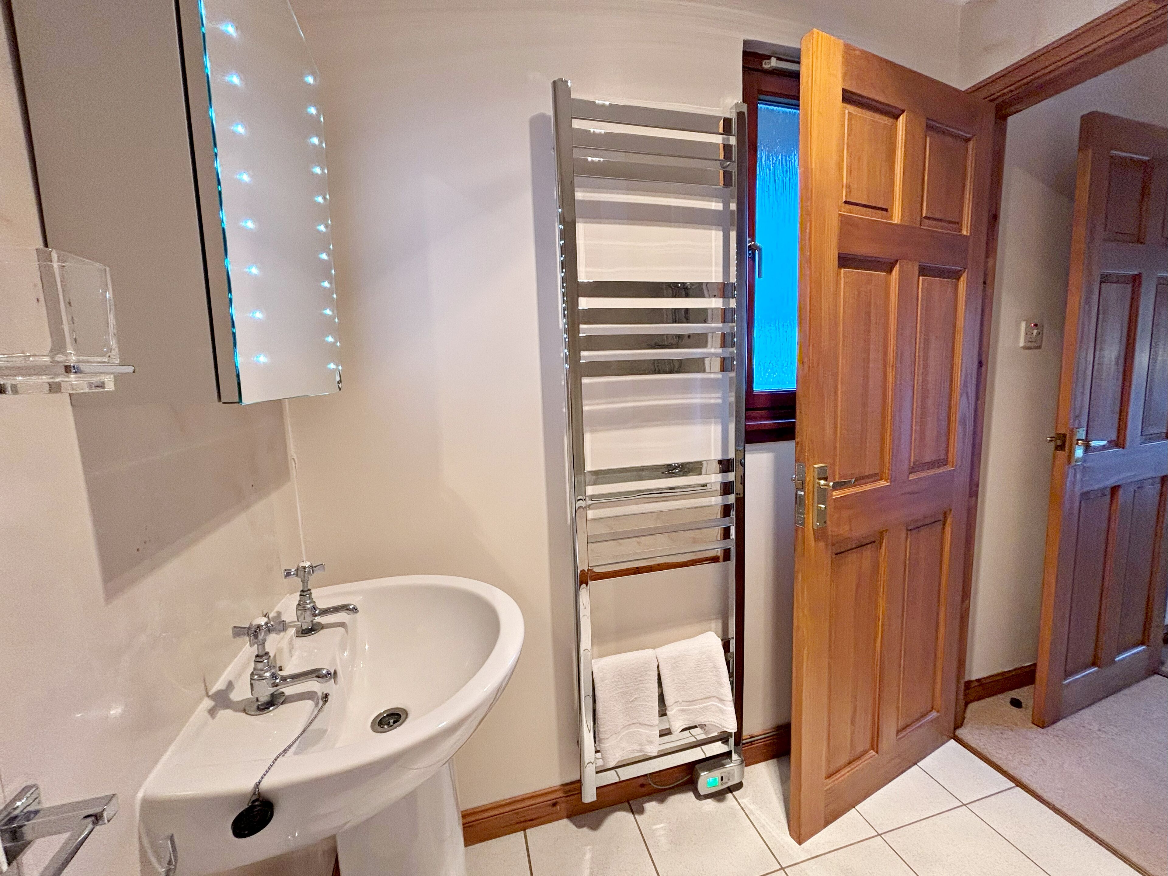 Een badkamer met een wastafel, spiegel, handdoekrek en houten deur.