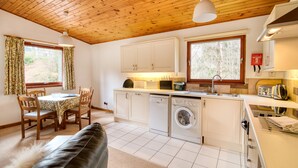 Une cuisine compacte avec un plafond en bois, des armoires blanches, un lave-linge et un coin repas comprenant une table et des chaises.