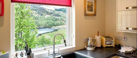 A kitchen with a sink, a window with a red blind, a toaster, and a painting on the wall.