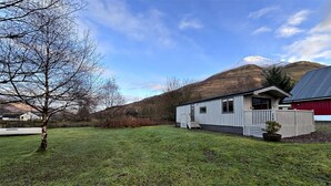 Ein eingeschossiges Mobilheim mit kleiner Veranda, einem Rasen und einem Berg im Hintergrund.