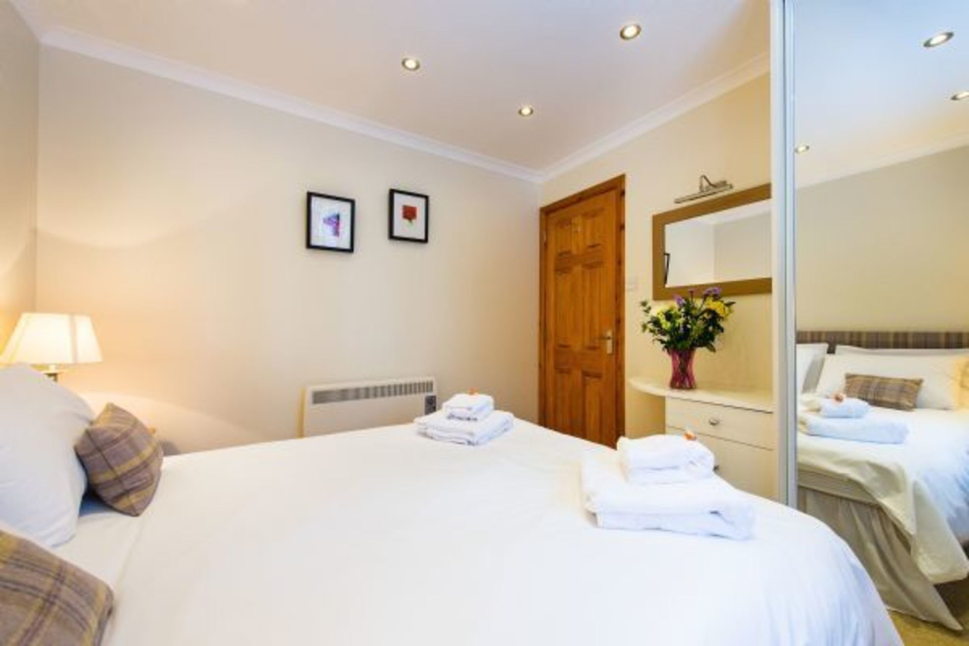 Una habitación de hotel con una cama grande, una mesita de noche con lámpara, una puerta de madera y un espejo en la pared.
