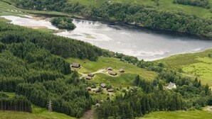 A rural landscape with a river, dense forest, and several small houses. - The Osprey (Crianlarich)
