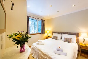 Habitación de hotel con cama, lámparas de noche, ventana con cortinas, un florero con flores y una cámara de seguridad instalada en la pared.