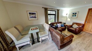 A living room with a glass table, leather sofas, and a wooden door. - The Osprey (Crianlarich)