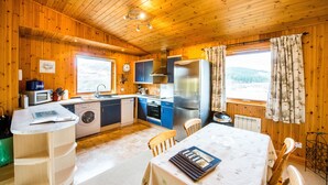 Une cuisine aménagée dans une cabane en bois, comprenant un coin repas, un lave-linge et un réfrigérateur.