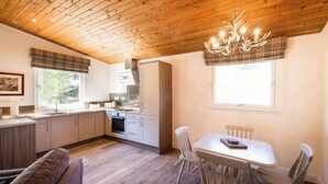 A modern kitchen with wooden ceiling, a dining area with white chairs, and a sofa. - The Stalker (Crianlarich)