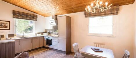 Una cocina moderna con techo de madera, una zona de comedor con sillas blancas y un sofá.