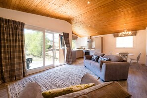 Amplia sala de estar con techo de madera, un conjunto de sofás, una mesa de comedor y vistas a través de amplios ventanales.