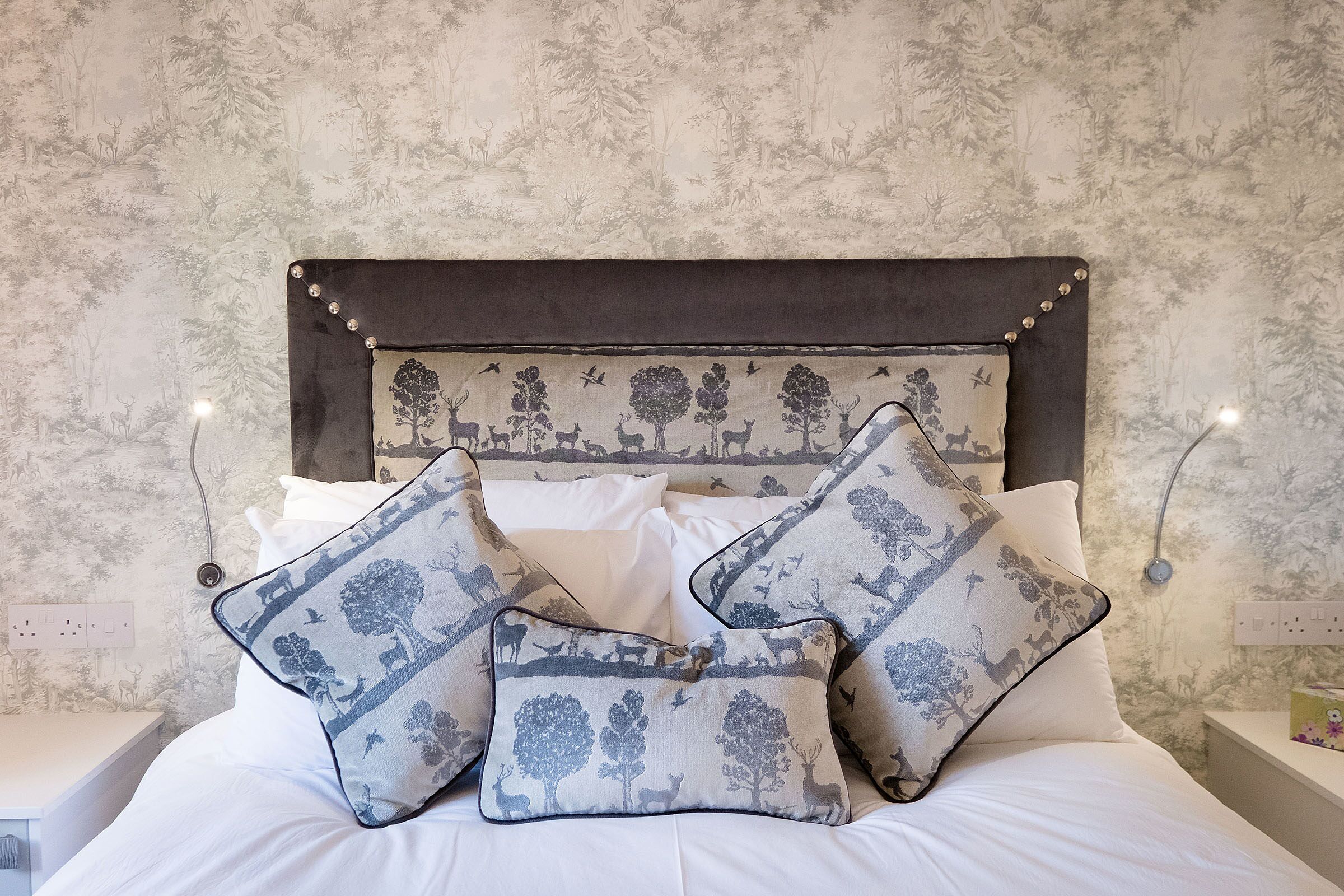 A bed with white bedding and decorative pillows featuring a nature scene.