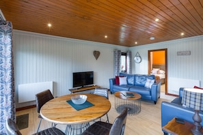 Ein gemütliches Wohnzimmer mit Holzboden, einem blauen Sofa, einem Fernseher und einem Essbereich mit rundem Tisch.