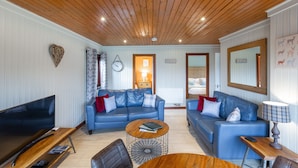 Ein Wohnzimmer mit Holzboden, zwei blaue Sofas, einem Couchtisch, einem Fernseher und einer Lampe.
