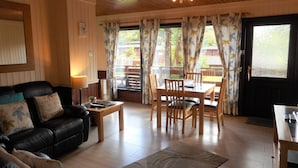 A cozy living room with a black leather sofa, a wooden coffee table, and a dining area with a table and chairs. - Birch Lodge 13 with Hot Tub (Newton Stewart)