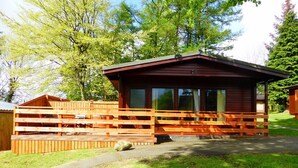 A wooden cabin with a porch and a covered deck area. - Birch Lodge 13 with Hot Tub (Newton Stewart)
