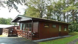 A wooden cabin with a porch, a fenced deck, and a number 13 sign. - Birch Lodge 13 with Hot Tub (Newton Stewart)