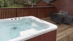 A hot tub on a wooden deck with a table and chairs nearby. - Birch Lodge 19 with Hot Tub (Newton Stewart)