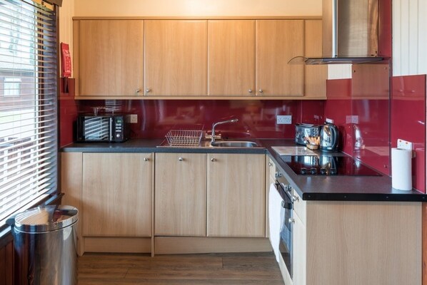 A compact kitchen with wooden cabinets, a stainless steel sink, and a red backsplash.